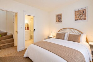 A hotel room with a bed, a nightstand, a wall-mounted lamp, a door leading to a bathroom, and a staircase. - Kensington 2-bed Mews House Next to Holland Park (London)