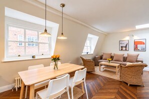 A modern living room with a dining area, featuring a herringbone wood floor, white furniture, and a brick wall. - Kensington 2-bed Mews House Next to Holland Park (London)