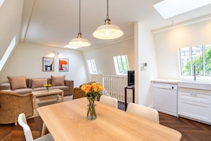 A modern kitchen with white cabinets, a wooden dining table, and a view of greenery outside. - Kensington 2-bed Mews House Next to Holland Park (London)
