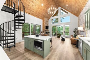 Una cocina moderna con una isla central, una escalera de caracol y grandes ventanales con vistas al exterior.