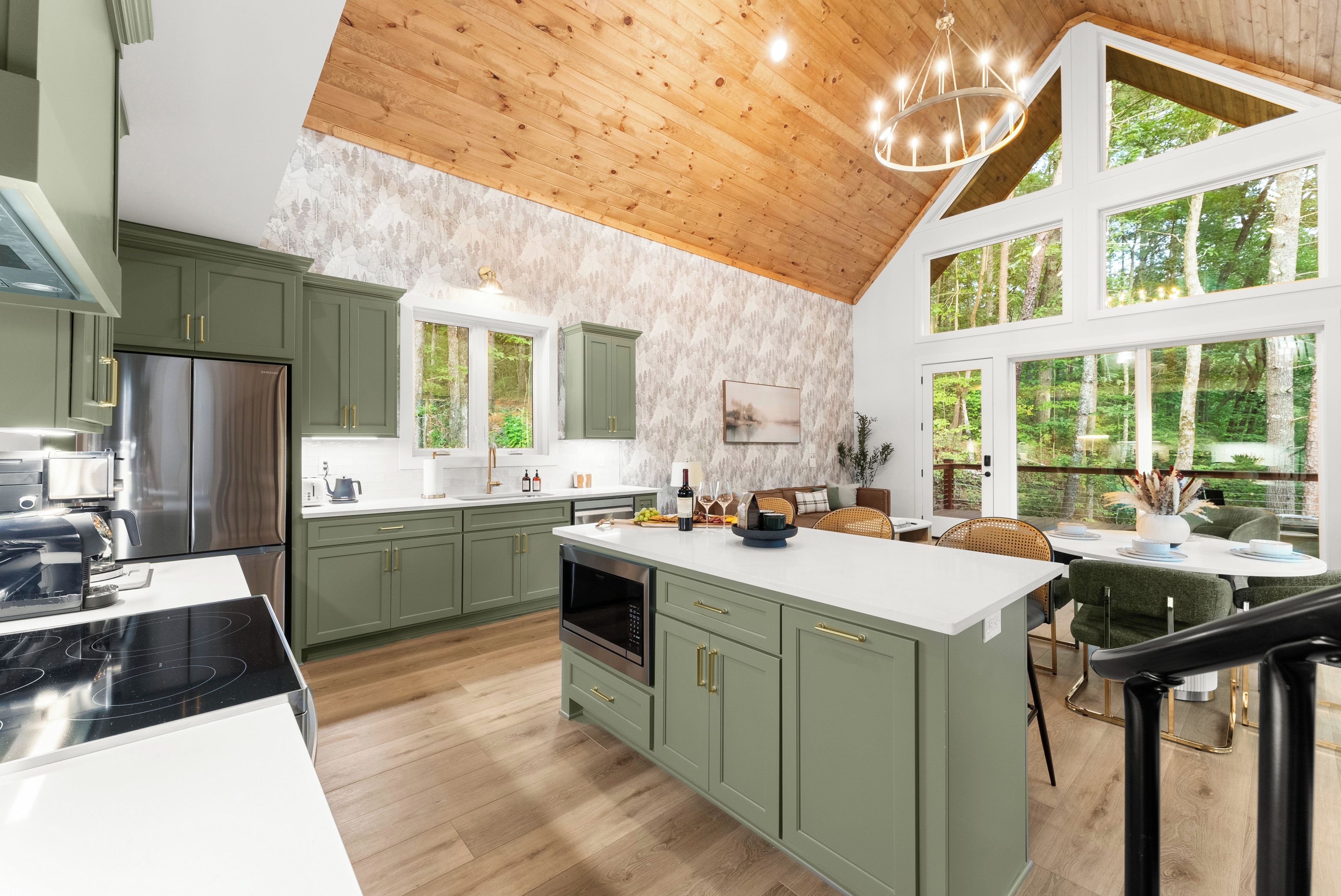 A modern kitchen with green cabinets, a stainless steel refrigerator, and a large island with a built-in oven.