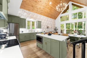 A modern kitchen with green cabinets, a stainless steel refrigerator, and a large island with a built-in oven.