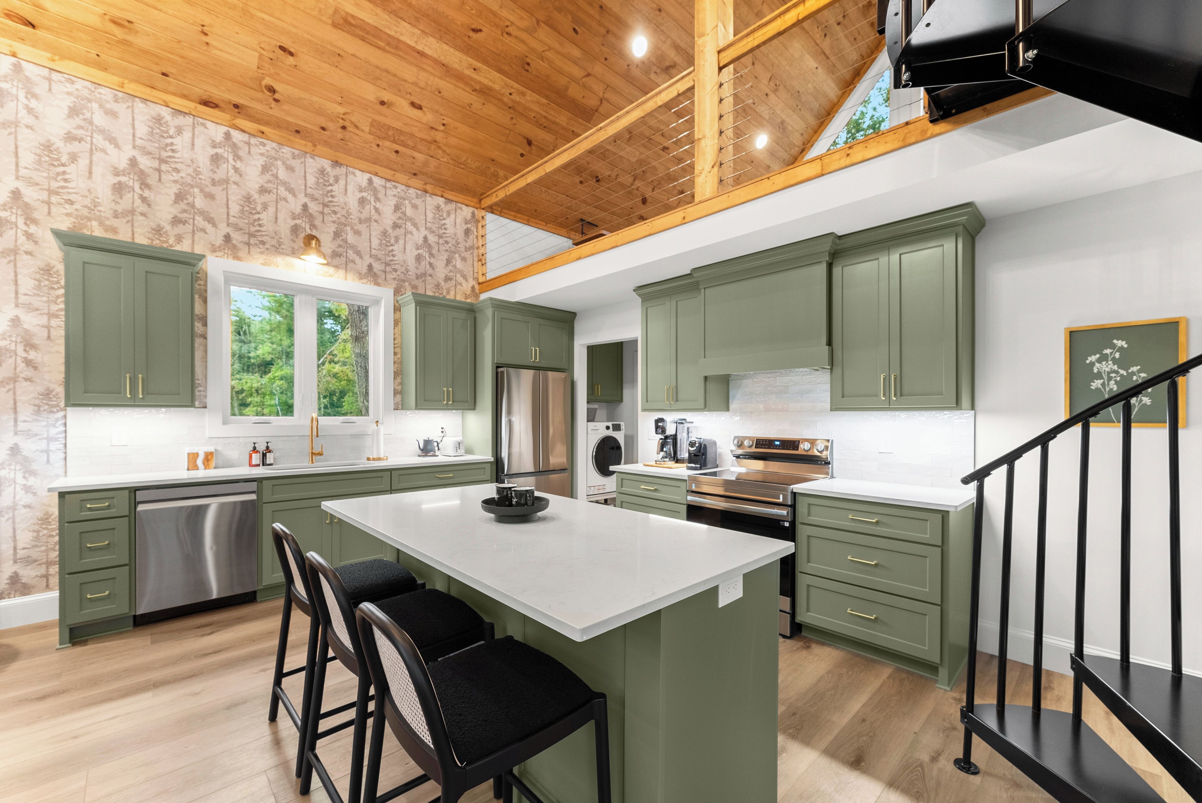 A kitchen with green cabinets, a large island, stainless steel appliances, and a wooden ceiling.