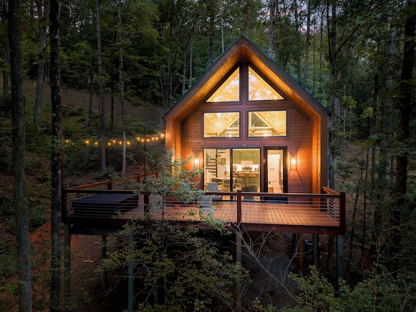 Una cabaña de madera con un balcón, ventanas grandes y una escalera que lleva a la entrada.