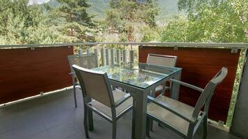 A glass-top table with four chairs on a balcony with a view of trees and mountains.