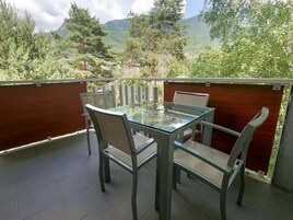 Ein Glastisch mit vier Stühlen auf einem Balkon mit Blick auf Bäume und Berge.