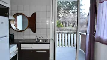 Une cuisine compacte équipée d’un évier, d’un miroir et d’une fenêtre donnant sur un balcon avec vue sur les arbres.