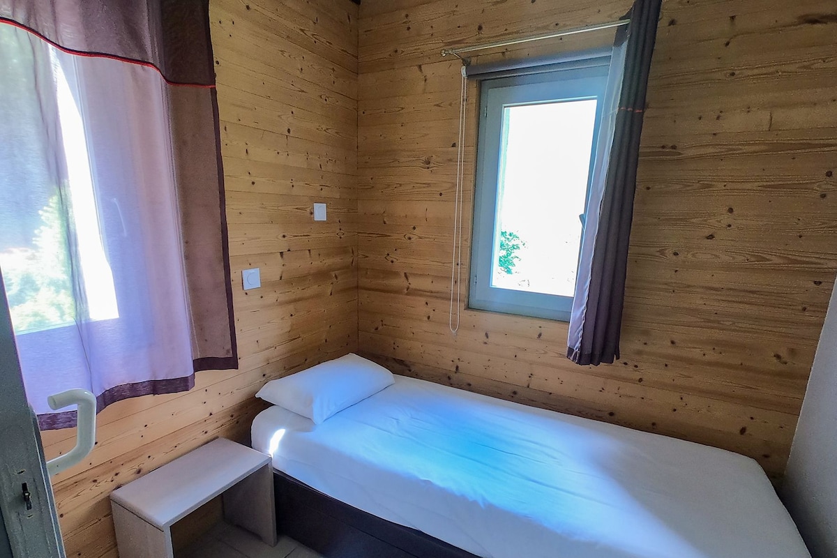 Una habitación pequeña con cama individual, ventana, mesita de noche y cortina.