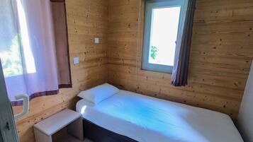 A small, single-bed room with a window, a bedside table, and a curtain.