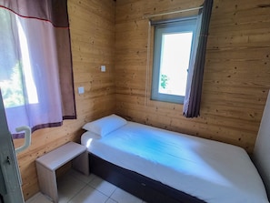 Una habitación pequeña con cama individual, ventana, mesita de noche y cortina.