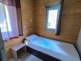 Ein kleines Zimmer mit einem Einzelbett, einem Fenster, einem Nachttisch und einem Vorhang.
