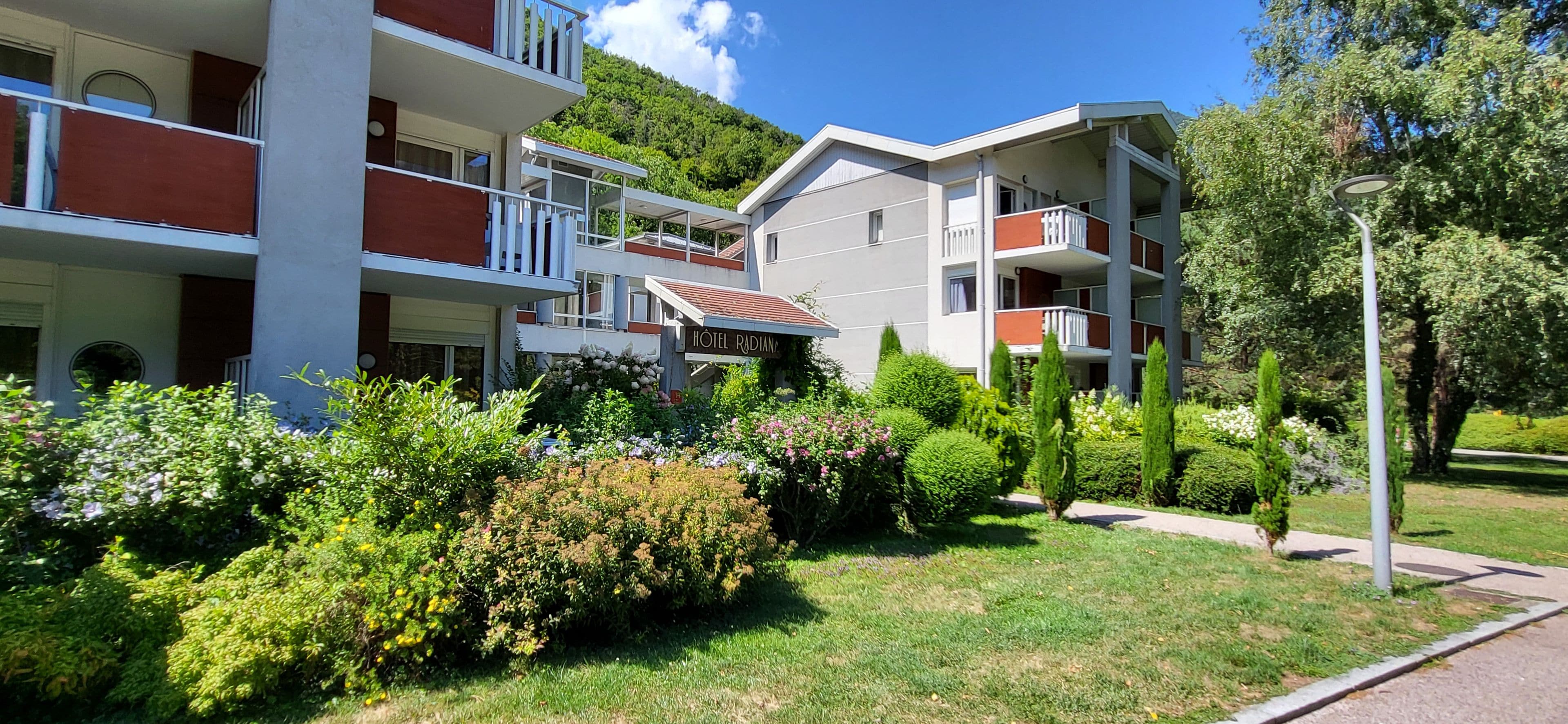 A hotel with multiple balconies, a garden with various plants, and a clear sky.