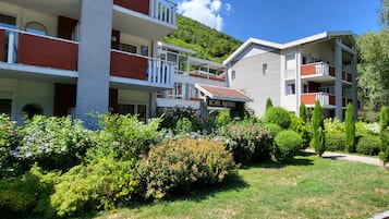 A hotel with multiple balconies, a garden with various plants, and a clear sky.