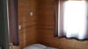Un lit simple dans une chambre de cabane en bois, avec une fenêtre et des rideaux.