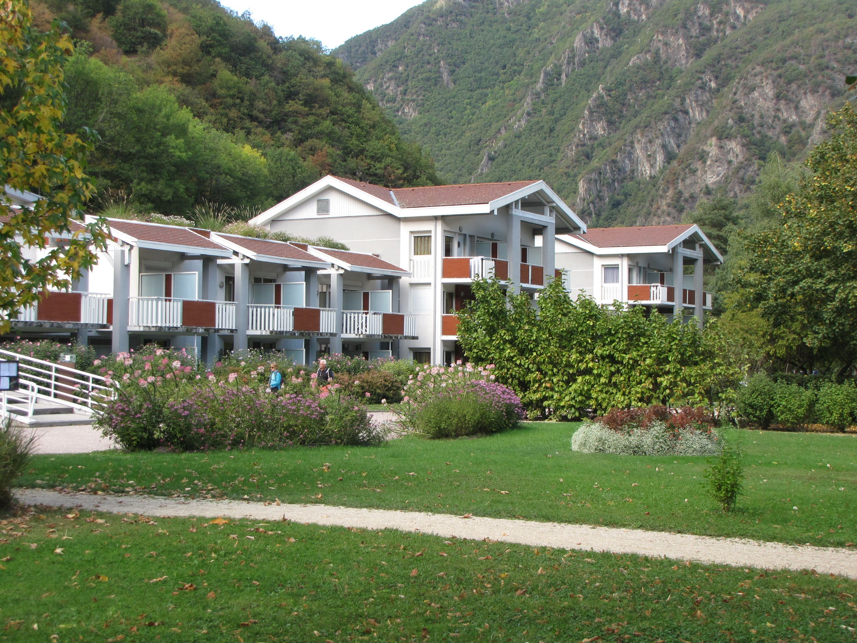 A hotel with multiple floors, balconies, and a garden area with various plants.