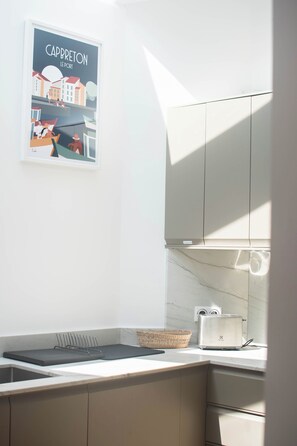 Una cocina con encimera blanca, un tostador, una cesta y un cartel enmarcado en la pared.