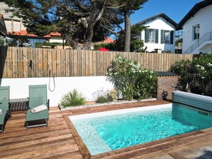 En swimmingpool med en træterrasse, omgivet af et træhegn og grønt vegetation.