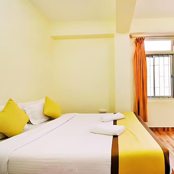 Una habitación de hotel con una cama, almohadas, un ventanal con cortinas y una mesita de noche.