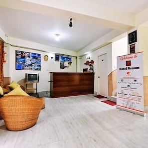 Zona de recepción de un hotel, con mostrador, televisor y cartel de bienvenida.