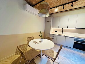 A modern kitchen with white cabinets, a round dining table with cushioned chairs, and a hanging light fixture. - Apartment in Eixample (Barcelona)
