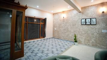 A room with a patterned floor, a window with blinds, a wall-mounted light fixture, and a framed picture.