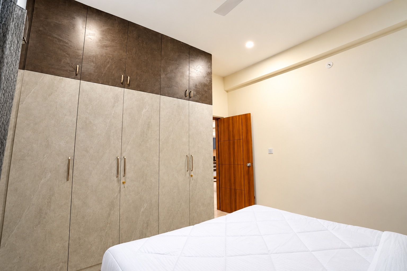 A bedroom with a bed, a wardrobe with multiple doors, and a wooden door in the background.