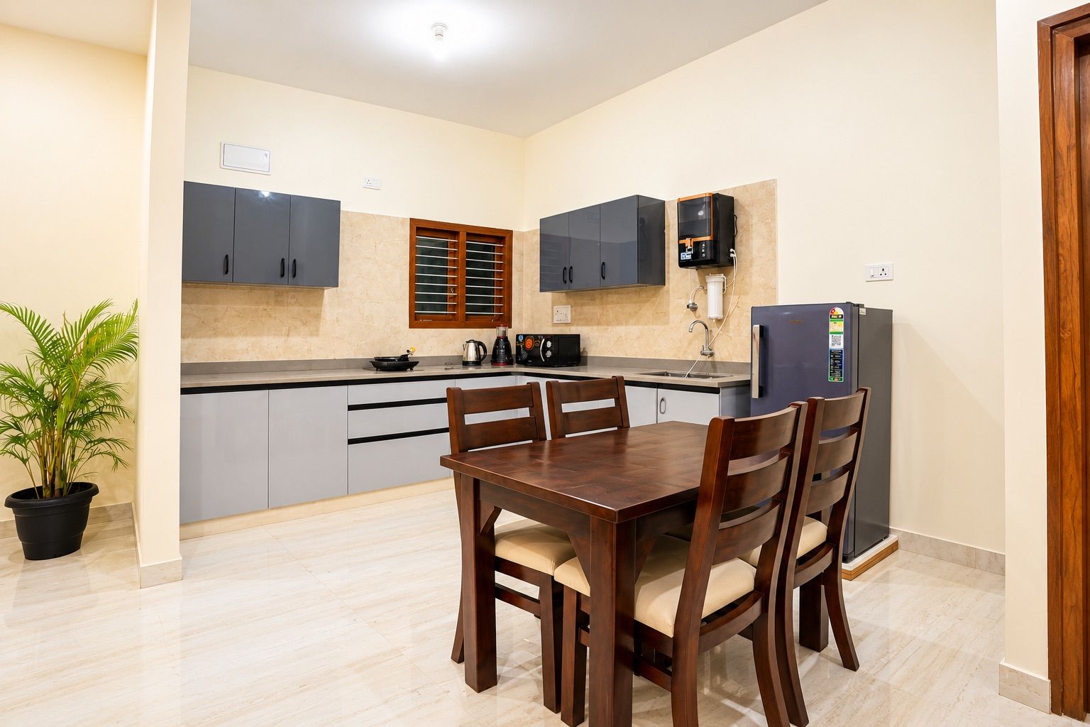 A modern kitchen with grey cabinets, a dining table with chairs, a refrigerator, and a potted plant.