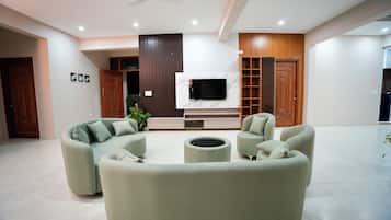 A modern living room with a curved sofa set, a flat-screen TV mounted on a marble wall, and a wooden cabinet with glass doors.