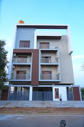 A multi-story building with balconies, a gated entrance, and a signboard.