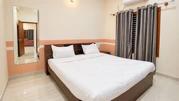 Habitació d'hotel amb un llit, un mirall, un aparell d'aire condicionat i una finestra amb cortines.