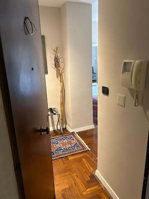 Ein Flur mit einer Holztür, einem gemusterten Teppich, einem an der Wand montierten Telefon und einer Zierpflanze.