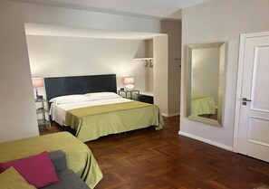 A hotel room with two beds, a bedside table with a lamp, a mirror on the wall, and a door. - MANETTI ROOMS Double Room on Via Chiaia, 600 meters from the waterfront. (Napoli)