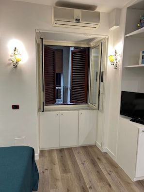Ein gemütlicher Raum mit integriertem Fernseher, einem Fenster mit Rollläden und einer Decken-Klimaanlage.