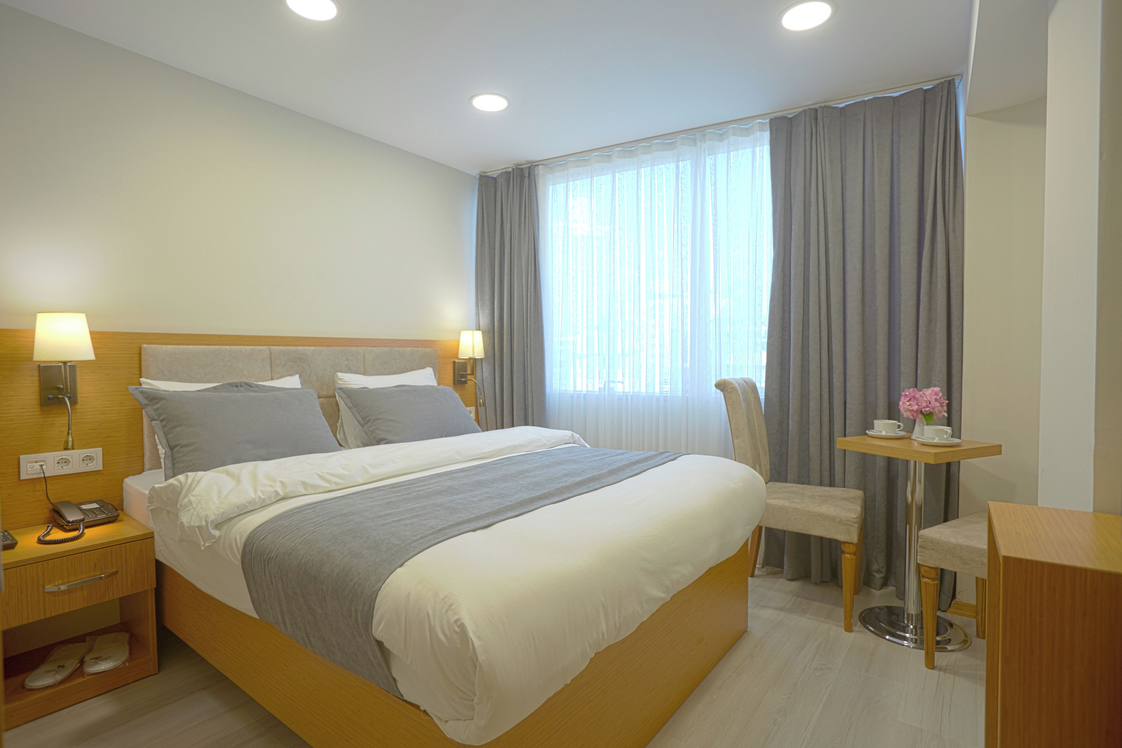 A hotel room with a large bed, bedside lamps, a desk with a chair, and a window with curtains.