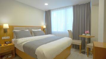 A hotel room with a large bed, bedside lamps, a desk with a chair, and a window with curtains.