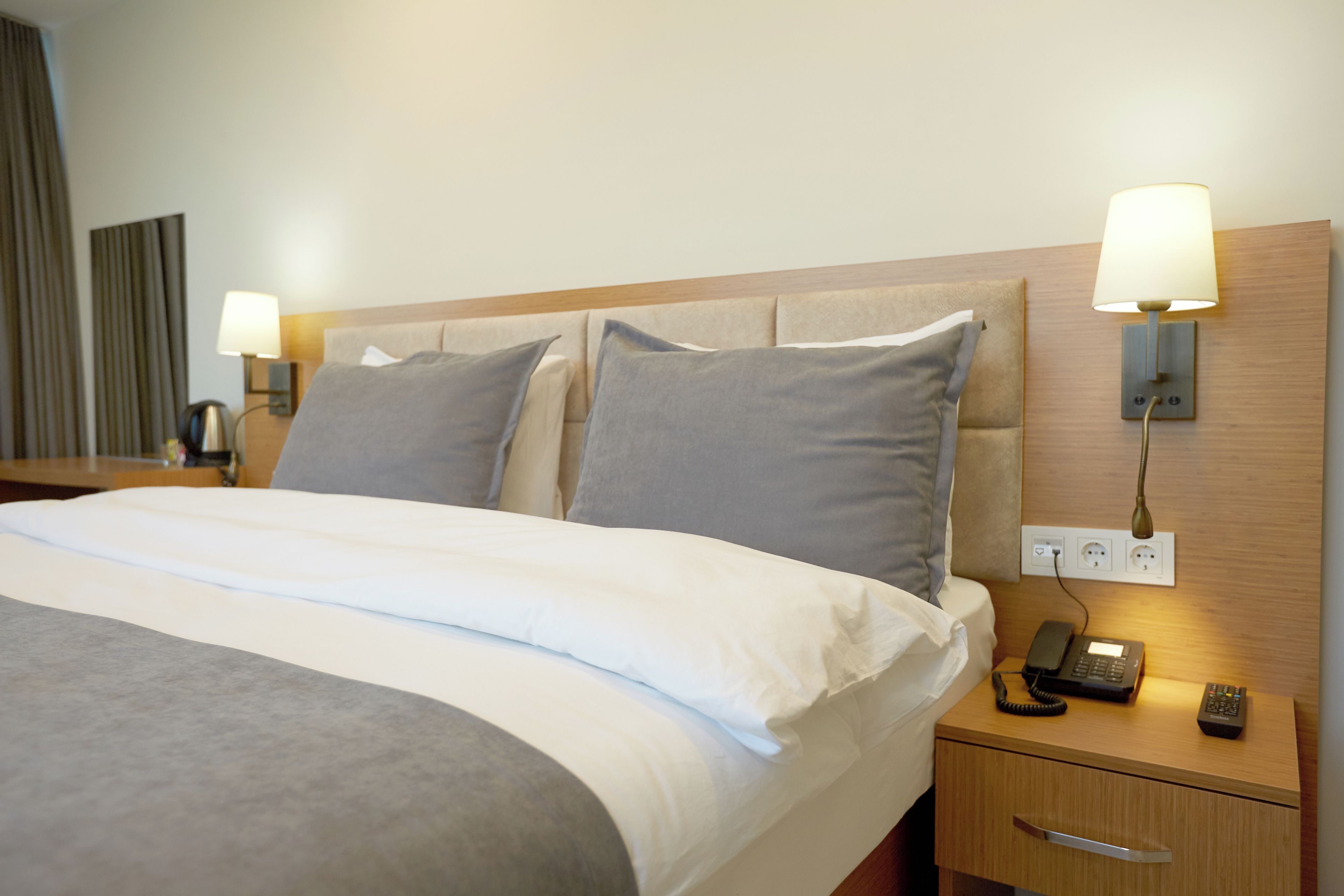 Ein Hotelzimmer mit einem ordentlich bezogenen Bett, Nachttischlampen, einem Telefon und einem Nachttisch.