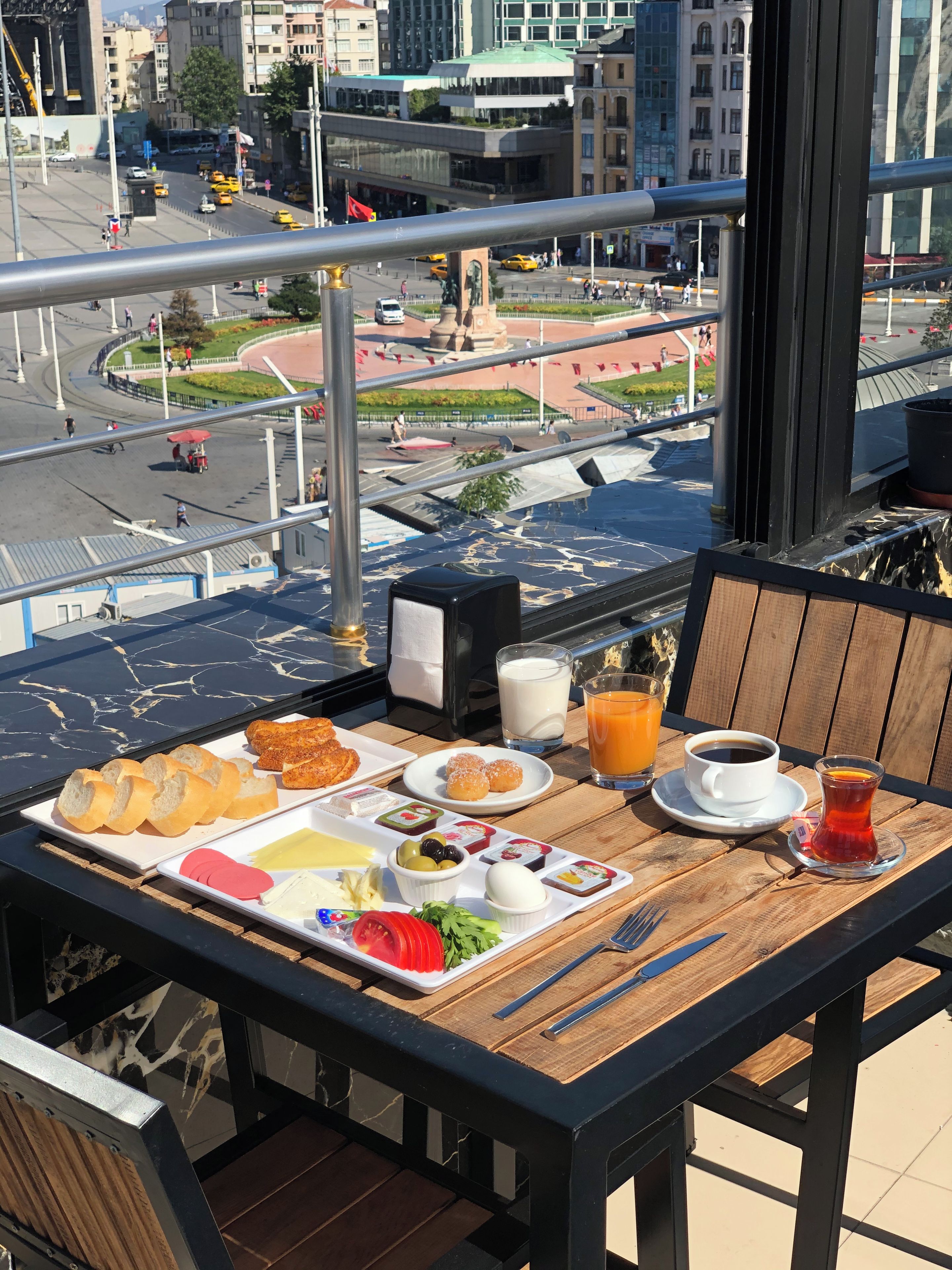 A balcony table with breakfast items, a city view, and a modern urban setting.