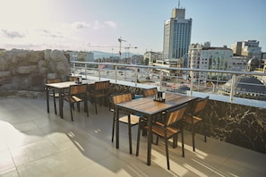 An outdoor seating area with tables and chairs, a stone wall, and a view of a cityscape with buildings and a crane. - Kartal Palace Taksim Square FAMILY HOTEL (Istanbul)