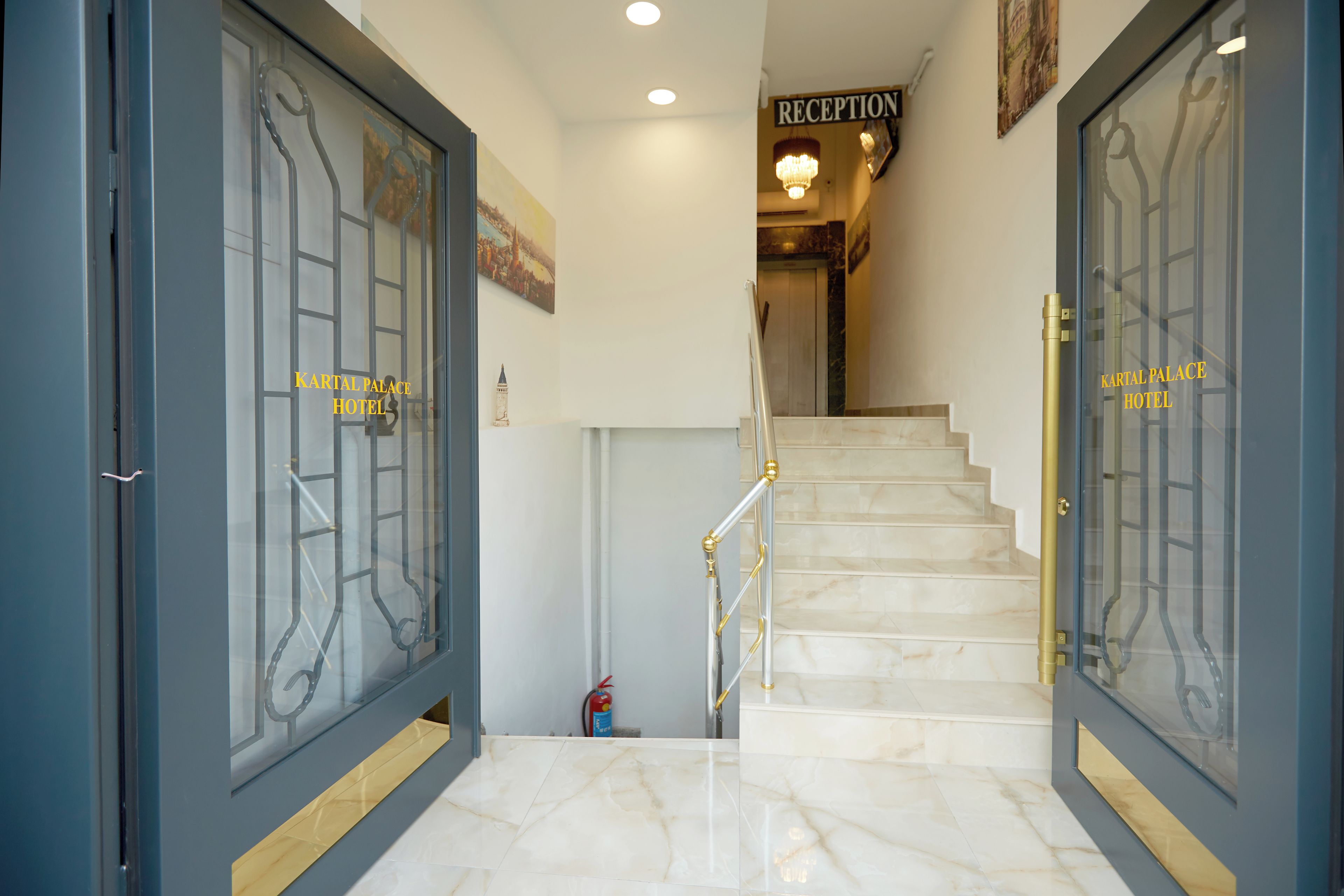 A hotel entrance with double doors, a reception sign, and a marble staircase.
