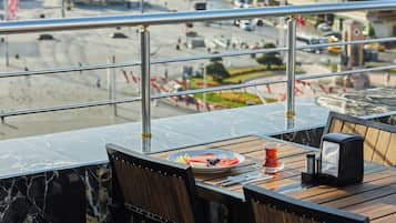 Un coin repas avec une table dressée pour deux, une vue sur la rue en contrebas et une rambarde au premier plan.
