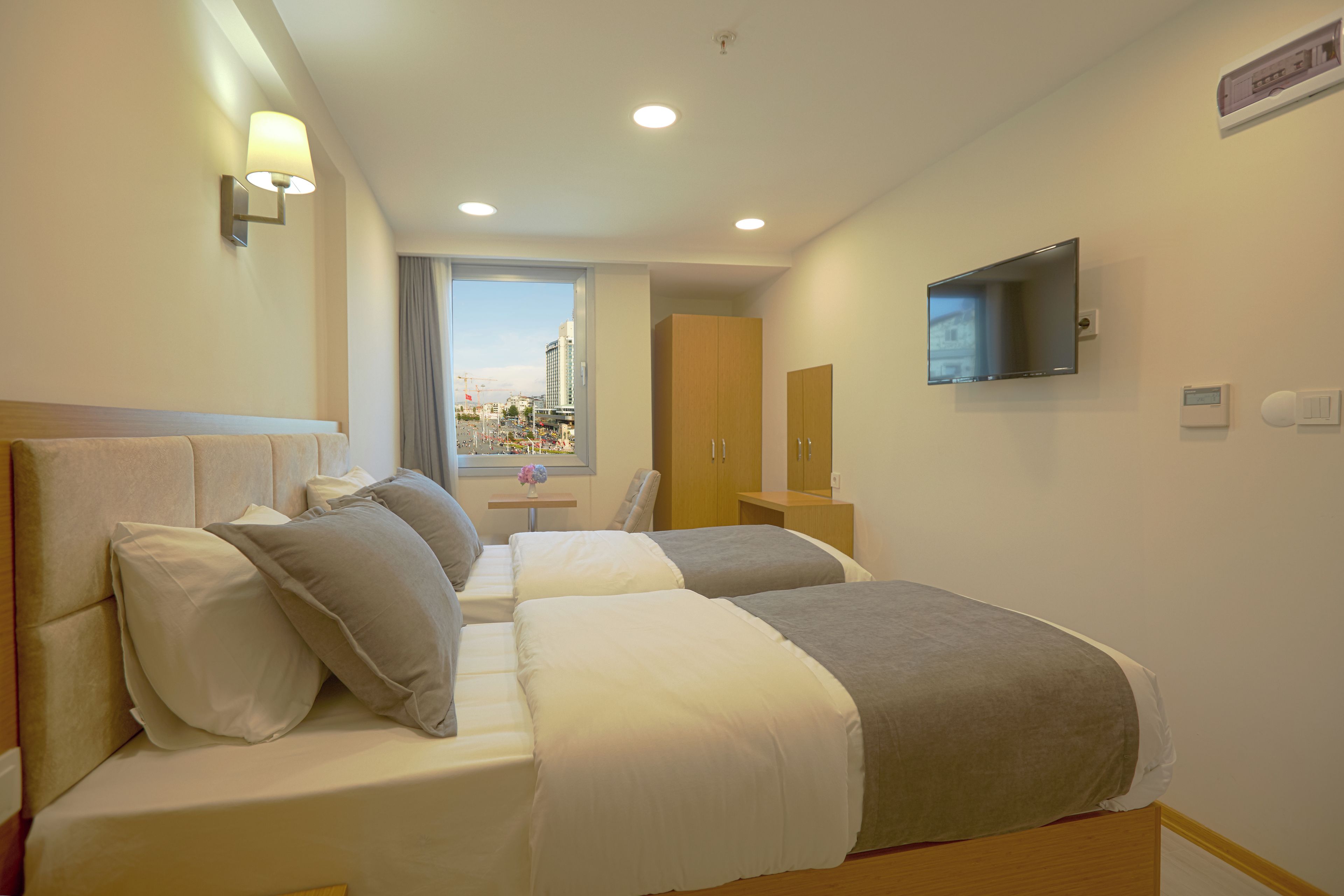 A hotel room with two beds, a TV, a window with a view of the city, and a desk with a chair.