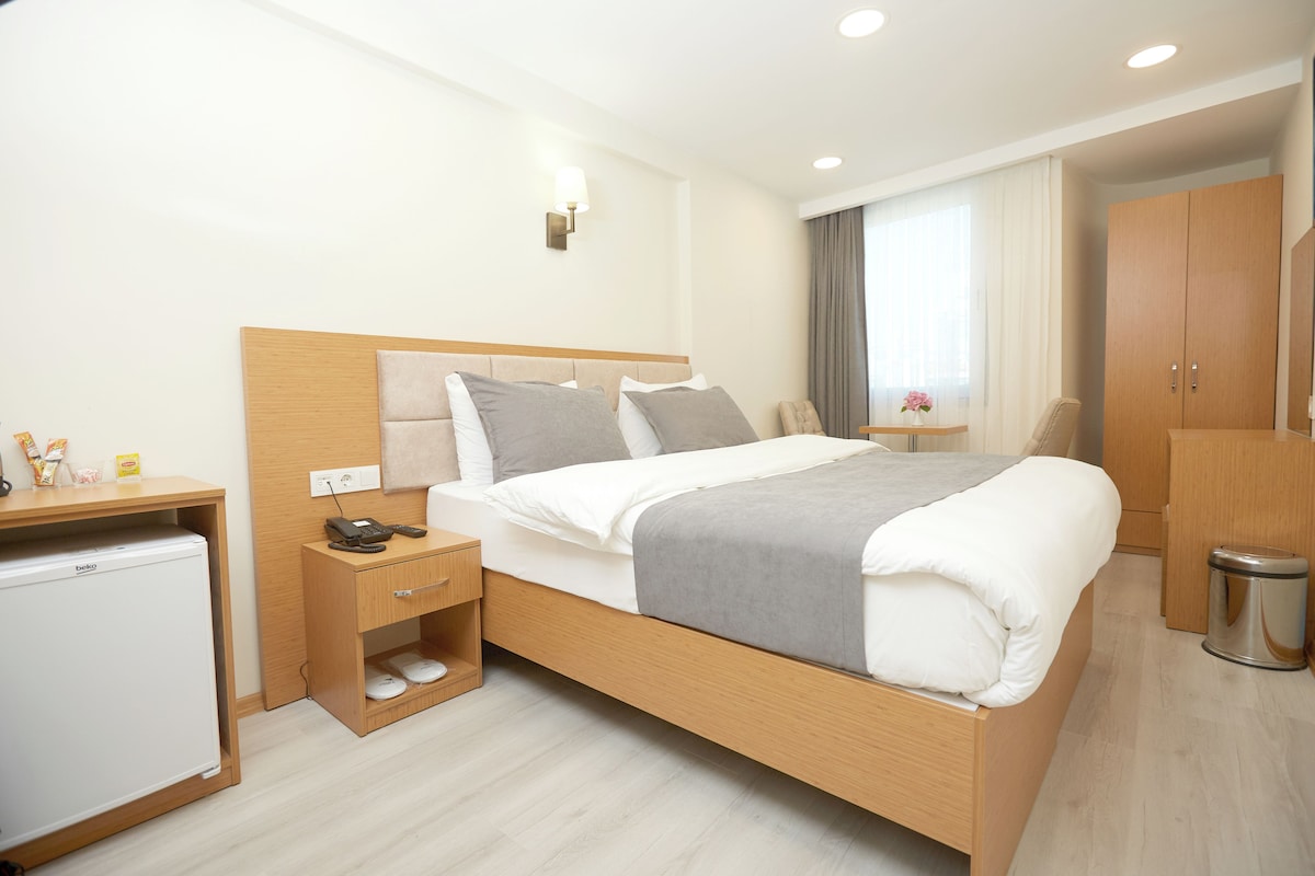 Una habitación de hotel moderna con cama de madera, mesita de noche y un refrigerador pequeño.