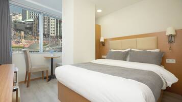 A hotel room with a bed, a desk, a chair, and a window with a city view.