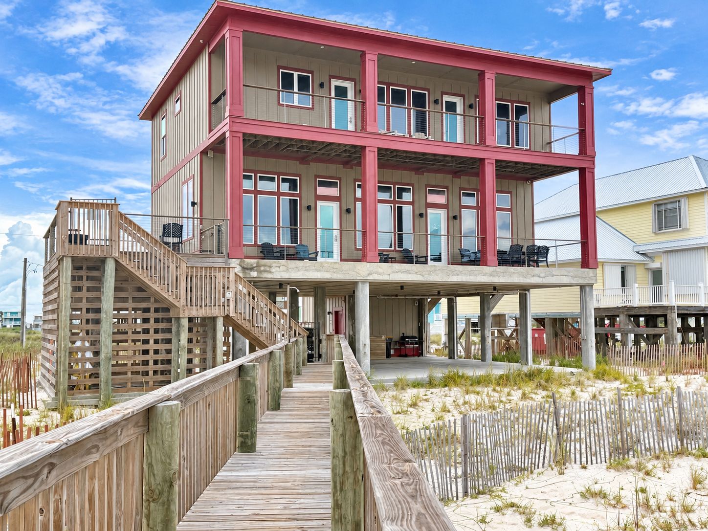 Ein mehrstöckiges Strandhaus mit einer Holzterrasse und einem überdachten Außenbereich.