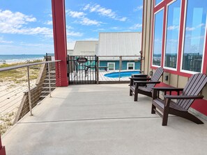 A balcony with a view of the beach, a pool, and a building with a red and white facade. - Coco Bella – Gulf Front Luxury | Private Pool | Sleeps 8 (Fort Morgan)