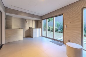 A spacious room with a large sliding glass door leading to a garden, a built-in kitchen area, and a small round table. - Domingos by Bhomy (São Paulo)