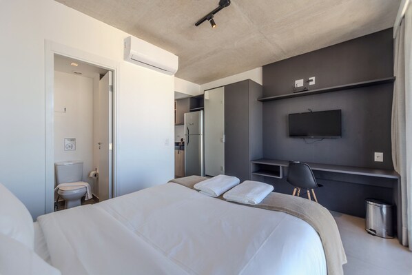 Una habitación de hotel moderna con una cama grande, un escritorio, un televisor y un baño.