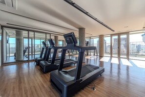 Un gimnasio con cintas de correr y equipo de ejercicio, ventanas amplias y vistas a la ciudad.