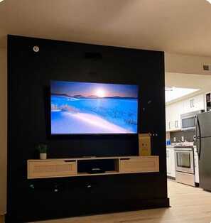 A flat-screen TV mounted on a black wall in a modern kitchen with white cabinets and stainless steel appliances. - The Cute Cozy Loft - 206 (Clarksville)