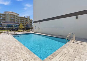 Ein rechteckiger Swimmingpool mit glasklar blauem Wasser, umgeben von einer gefliesten Terrasse.